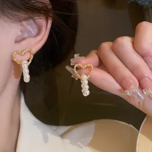 Detail view of gold heart-shaped earrings with hanging white pearls worn on ear