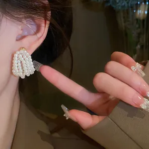 Close-up of woven pearl U-shaped drop earrings with a gold stud shown on an Asian model