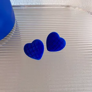 Dettaglio di orecchini a cuore blu Klein con texture in velluto trapuntato e perni.