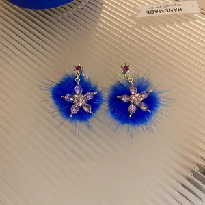Dettaglio di orecchini a fiore in pelliccia blu Klein con gemme viola scintillanti e rosse.