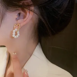 Close-up detail of golden hollow heart earrings featuring an elegant pearl drop design
