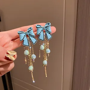 Dettaglio di orecchini a fiocco azzurro con strass neri e lunghe nappe dorate.