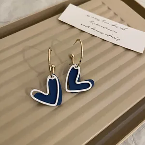 Dettaglio macro di orecchini a cuore blu Klein con design a contorno bianco minimalista.