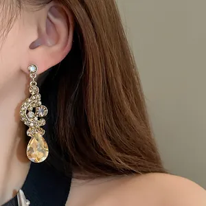 Close-up of elegant gold dangle earrings with sparkling rhinestones and teardrop gem.