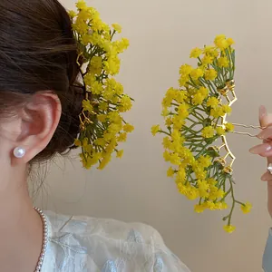 Detail view of yellow baby's breath flower hairpins shown on hair and held by hand