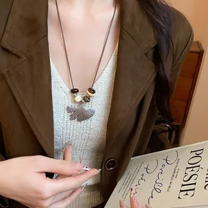 Detail view of a long sweater chain necklace with ginkgo leaf and wooden beads