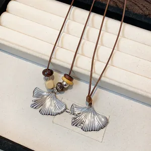 Detail view of textured silver ginkgo leaf pendants and decorative wood beads.