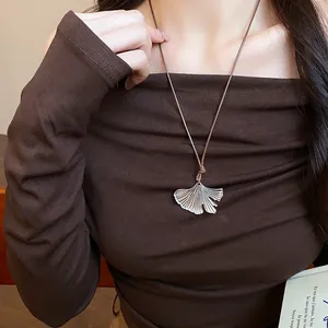 Detail shot of a textured silver ginkgo leaf pendant necklace on a brown cord worn by model.