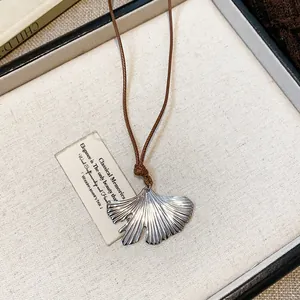 Detailed macro view of an elegant silver ginkgo leaf pendant necklace with brown cord