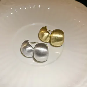 Close-up of minimalist brushed silver and gold bean stud earrings on a white plate