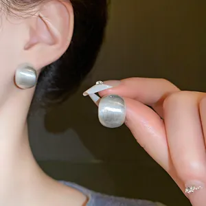 Close-up of silver-tone brushed geometric bean stud earrings with matte texture
