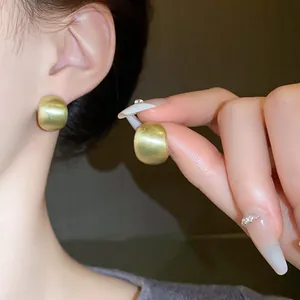 Detailed macro view showing the texture of gold brushed bean stud earrings worn and held.