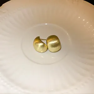 Close-up of golden brushed geometric bean stud earrings displayed on a white plate