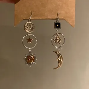 Detail of asymmetric sun and moon drop earrings with antique silver and gold finish.