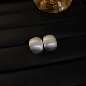 Close-up of matte silver brushed bean earrings with minimalist geometric design