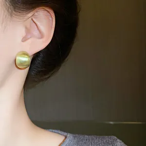 Close-up detail of a minimalist golden brushed geometric bean earring on model's ear