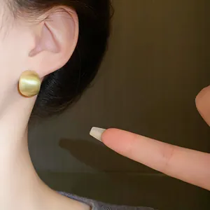 Detail shot of a matte gold brushed geometric bean stud earring on a model's ear