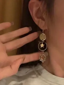 Close-up view showing details of asymmetric sun and moon dangle earrings worn on an ear
