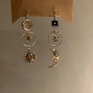 Detailed view of asymmetric celestial earrings featuring vintage sun and moon charms on silver hooks