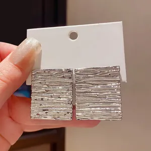 Macro detail of silver-toned square stud earrings with a unique wrinkled metal texture.