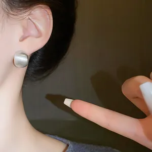 Detail view of a brushed silver bean stud earring showing minimalist geometric design