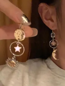Detailed view of asymmetric sun moon and star dangle earrings being worn and held