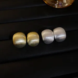 Detail of brushed gold and silver geometric bean stud earrings on a dark jewelry display