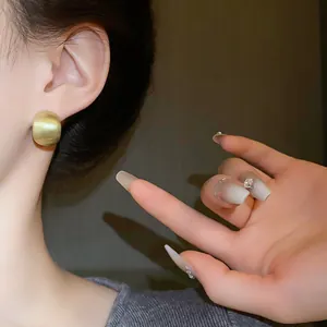 Close-up shot of elegant matte brushed golden geometric bean stud earrings on model