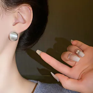 Close-up of minimalist brushed silver geometric stud earrings worn by a model.