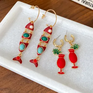 Détail macro de boucles d'oreilles en émail rouge poisson et verre à cocktail sur marbre