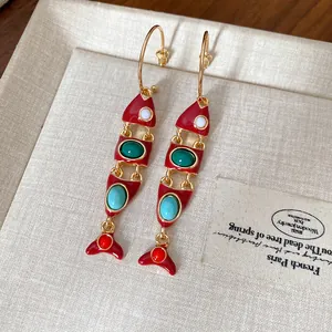 Gros plan de boucles d'oreilles pendantes poisson en émail avec pierres colorées vibrantes