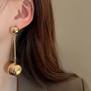 Minimalist gold metallic ball tassel earrings on model with silver needles.