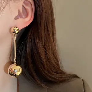 Close-up detail of stylish gold metallic double sphere tassel drop earrings worn by a model
