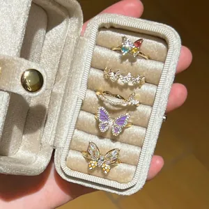 Variety of dainty butterfly rings with zircons and enamel in a beige velvet jewelry box.