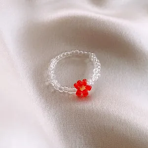 Detailed shot of a transparent beaded ring featuring a small red flower on soft fabric.