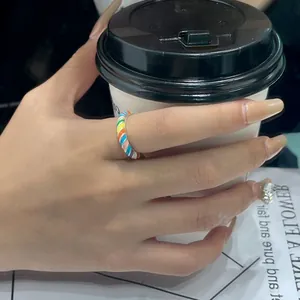 Detailed view of a colorful rainbow enamel twisted ring on a hand holding a coffee cup