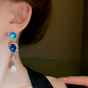 Close-up of vintage-style dangling earrings with blue gems and white pearl