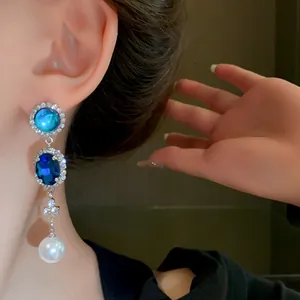 Close-up of elegant blue crystal and pearl drop earrings on a model, French retro style.
