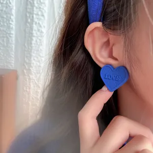 Close-up of Klein Blue heart-shaped earring with LOVE engraving on ear