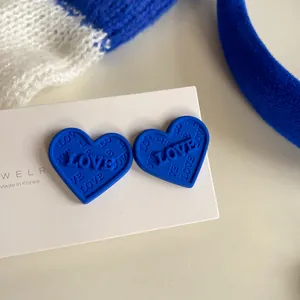 Macro view of Klein blue heart-shaped stud earrings with embossed LOVE lettering