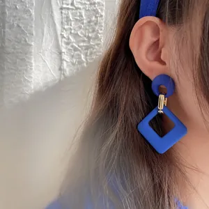 Close-up shot of retro Klein blue geometric square earrings worn by a female model.