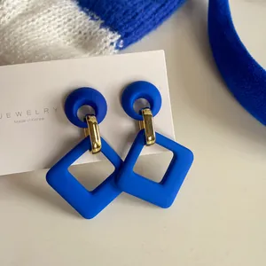 Close-up of Klein blue matte earrings featuring gold links and a retro square design.