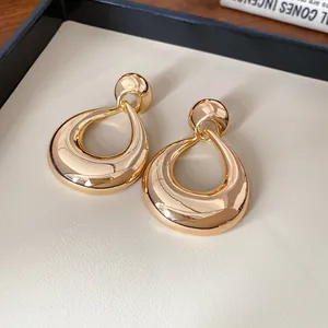 Détail rapproché de grandes boucles d'oreilles géométriques dorées sur un plateau blanc