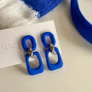 Close-up of matte Klein blue geometric earrings with gold link on jewelry display