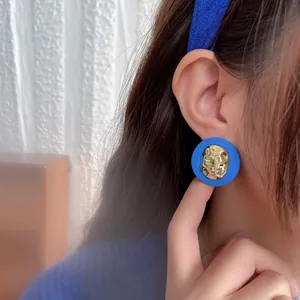 Close-up of Klein blue vintage stud earrings with hammered gold detail on model