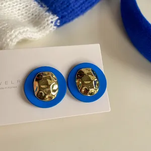 A detailed view of Klein blue stud earrings with a hammered gold-tone metal center