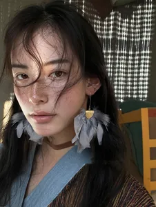 Detailed view of elegant grey feather tassel earrings worn by a model with warm lighting