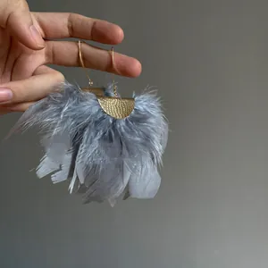 Close-up of grey feather tassel earrings with textured gold-tone metal hook detail.