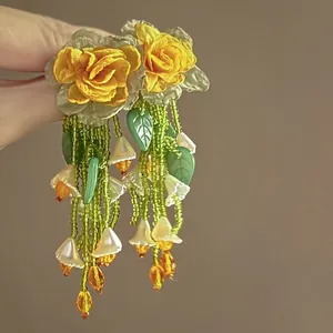 Detail shot of handcrafted yellow rose earrings with green bead tassels and flower charms.