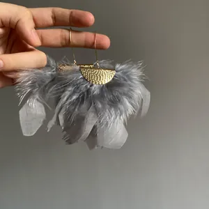 Hand-held detail view of elegant gray feather earrings with hammered gold semi-circle